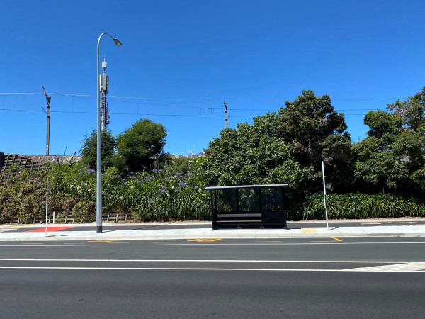 An empty stretch of road shows a road, cycle path, bus stop and footpath on a sunny day.