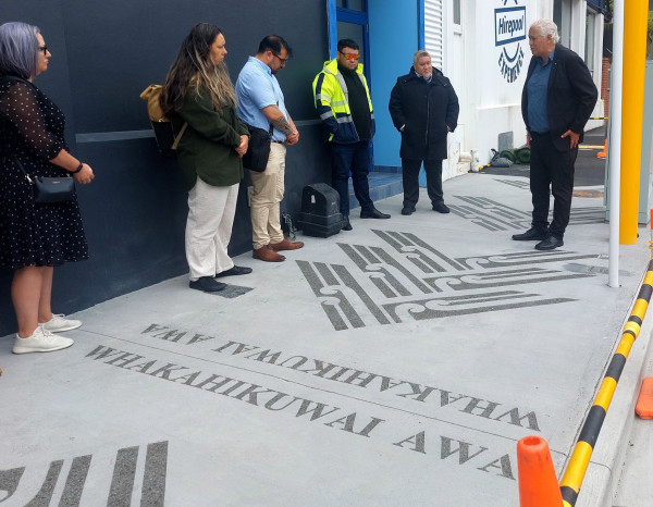 Six people stand around looking solemn by new markings showing a chevron design with koru and the words Whakahikuwai Awa etched into the pavement